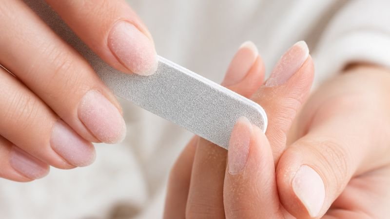 Nail technician gently filing gel nail polish before acetone removal