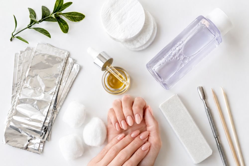 Gel nail polish removal tools including acetone, cotton pads, foil wraps, and nail file on a clean table