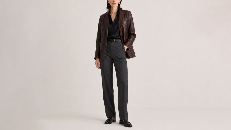 Make Every Outfit Count With a Brown Leather Jacket for Women Woman wearing a dark brown leather blazer with a black shirt, charcoal tailored trousers, and black loafers for a polished office outfit.