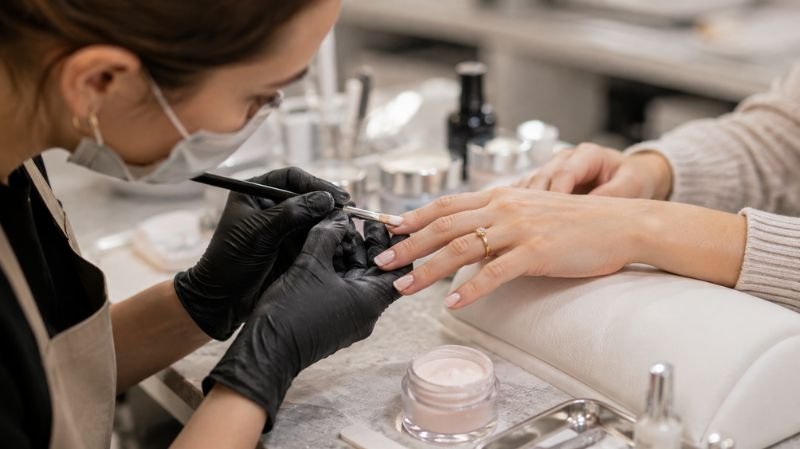 Nail technician creating short acrylic manicure in salon